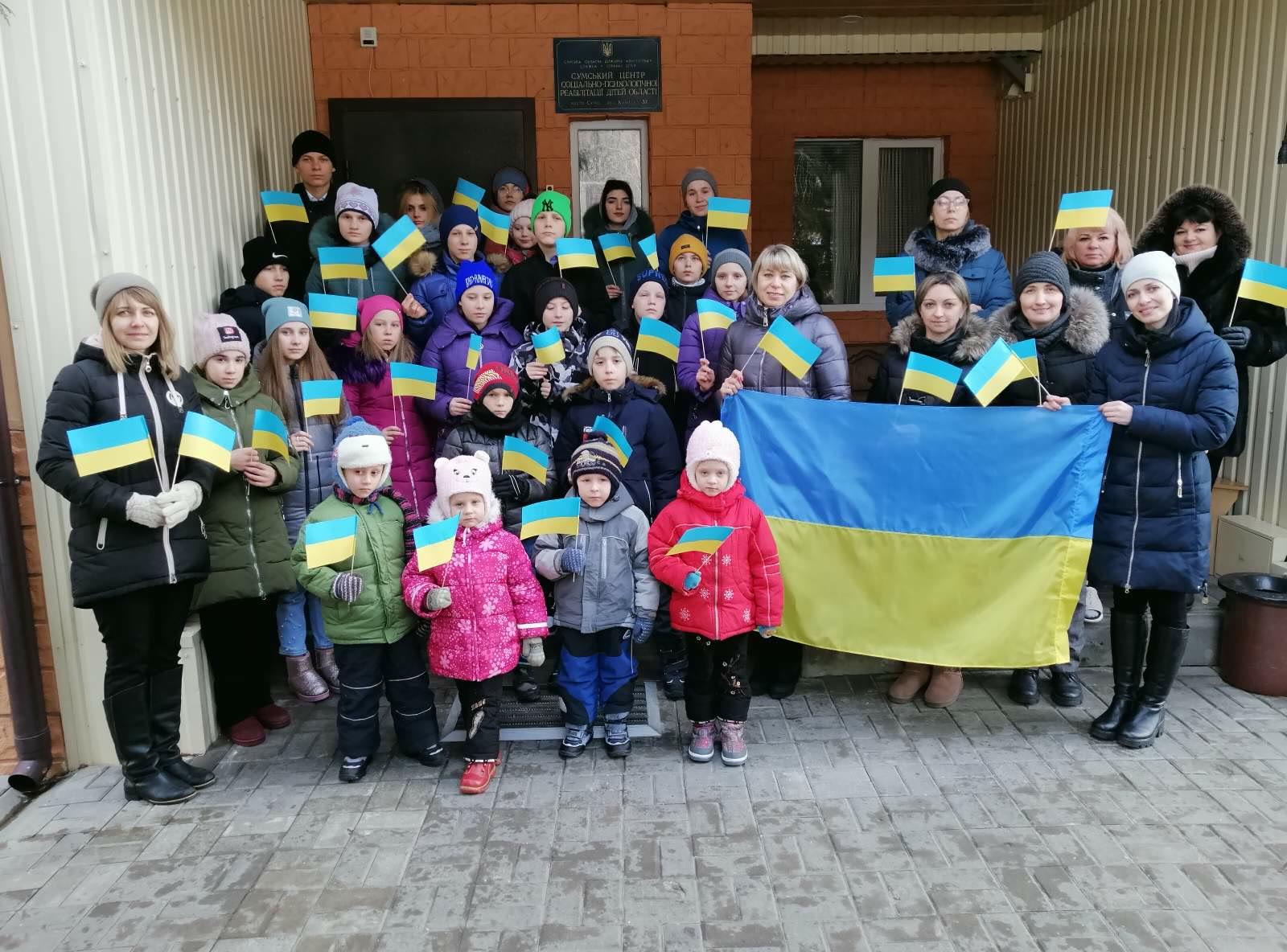 Children and caregivers gathered outdoors with Ukrainian flags